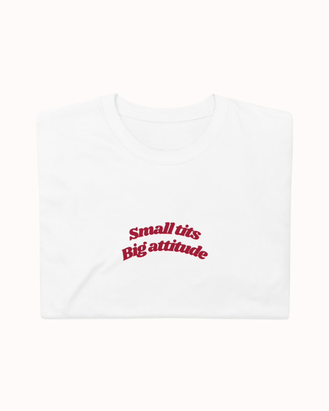 Folded White t-shirt featuring the ironic phrase "Small tits. Big attitude". Perfect for fans of funny merchandise, bold humor, and witty sarcasm.