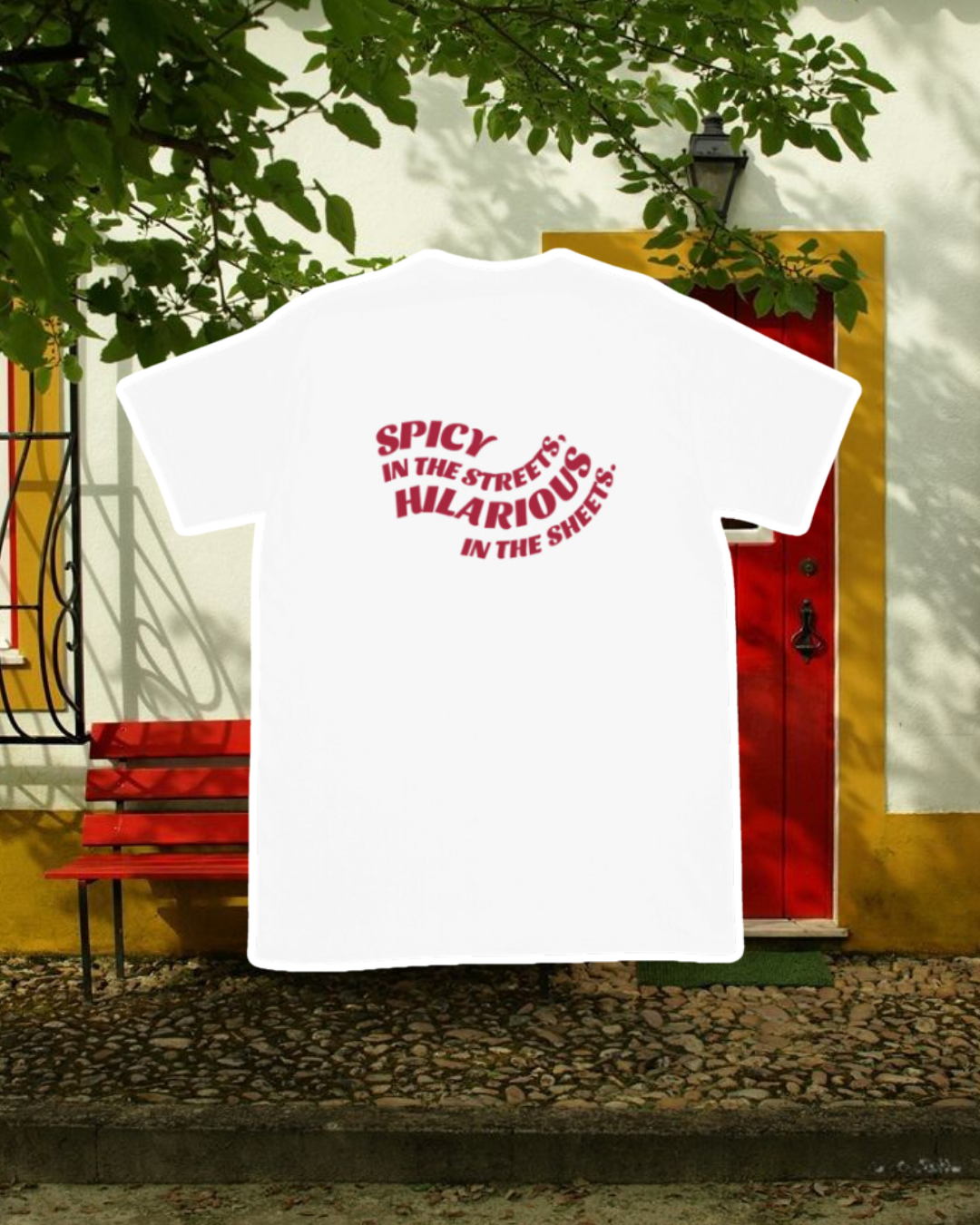 White T-Shirt with the phrase 'Spicy in the streets, Hilarious in the sheets' on the back, displayed against an inviting space, perfect for relaxation or gathering with friends. A playful and bold design for fans of funny merchandise and sarcasm.