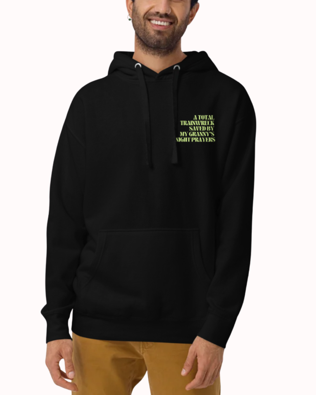 Front view of a Black hoodie worn by a smiling man, featuring the phrase "A total trainwreck saved my granny's night prayers" on the chest and back. Perfect for fans of funny merchandise, bold humor, and witty sarcasm.