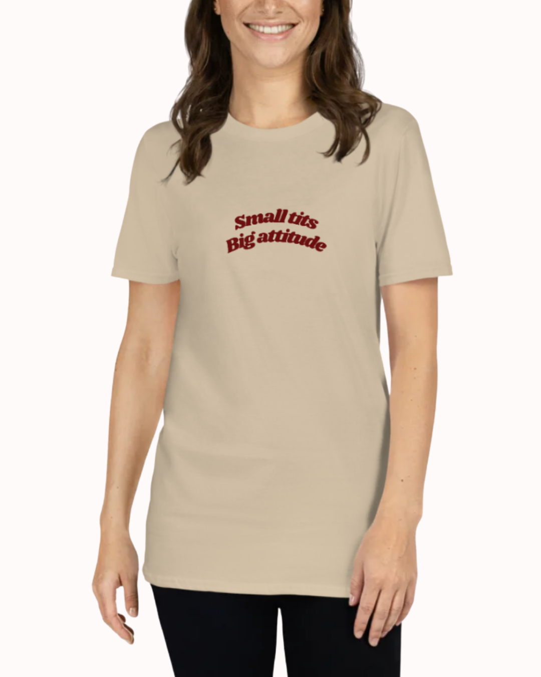 Front view of a Sand t-shirt worn by a smiling woman, featuring the phrase "Small tits. Big attitude" on the chest and back. Perfect for fans of funny merchandise, bold humor, and witty sarcasm.
