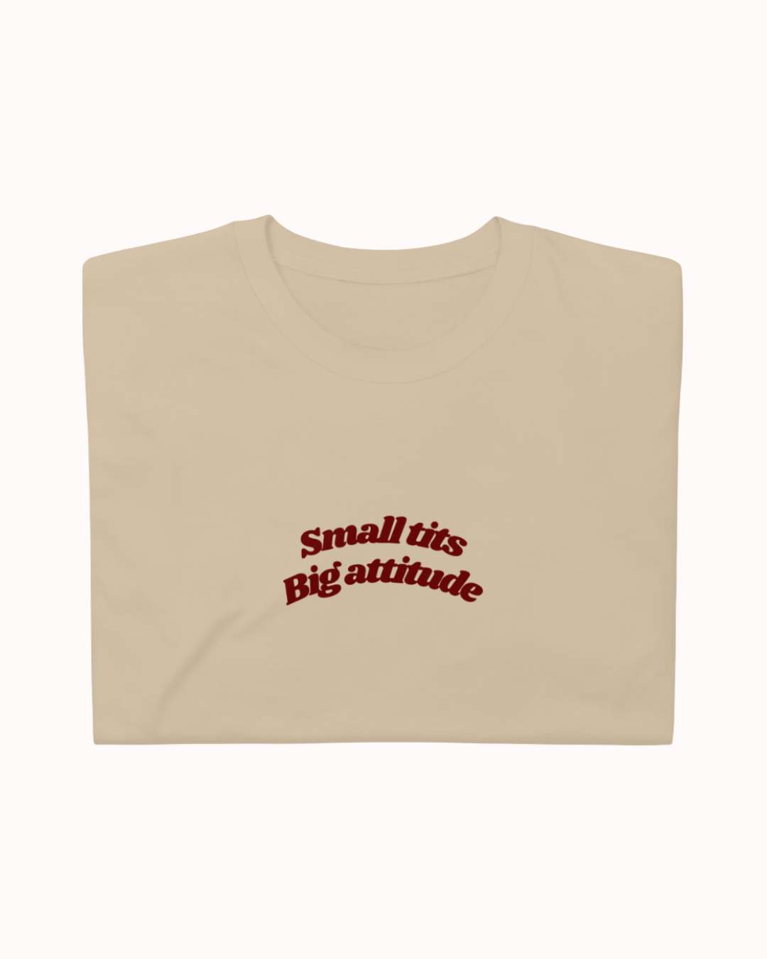 Folded Sand t-shirt featuring the ironic phrase "Small tits. Big attitude". Perfect for fans of funny merchandise, bold humor, and witty sarcasm.