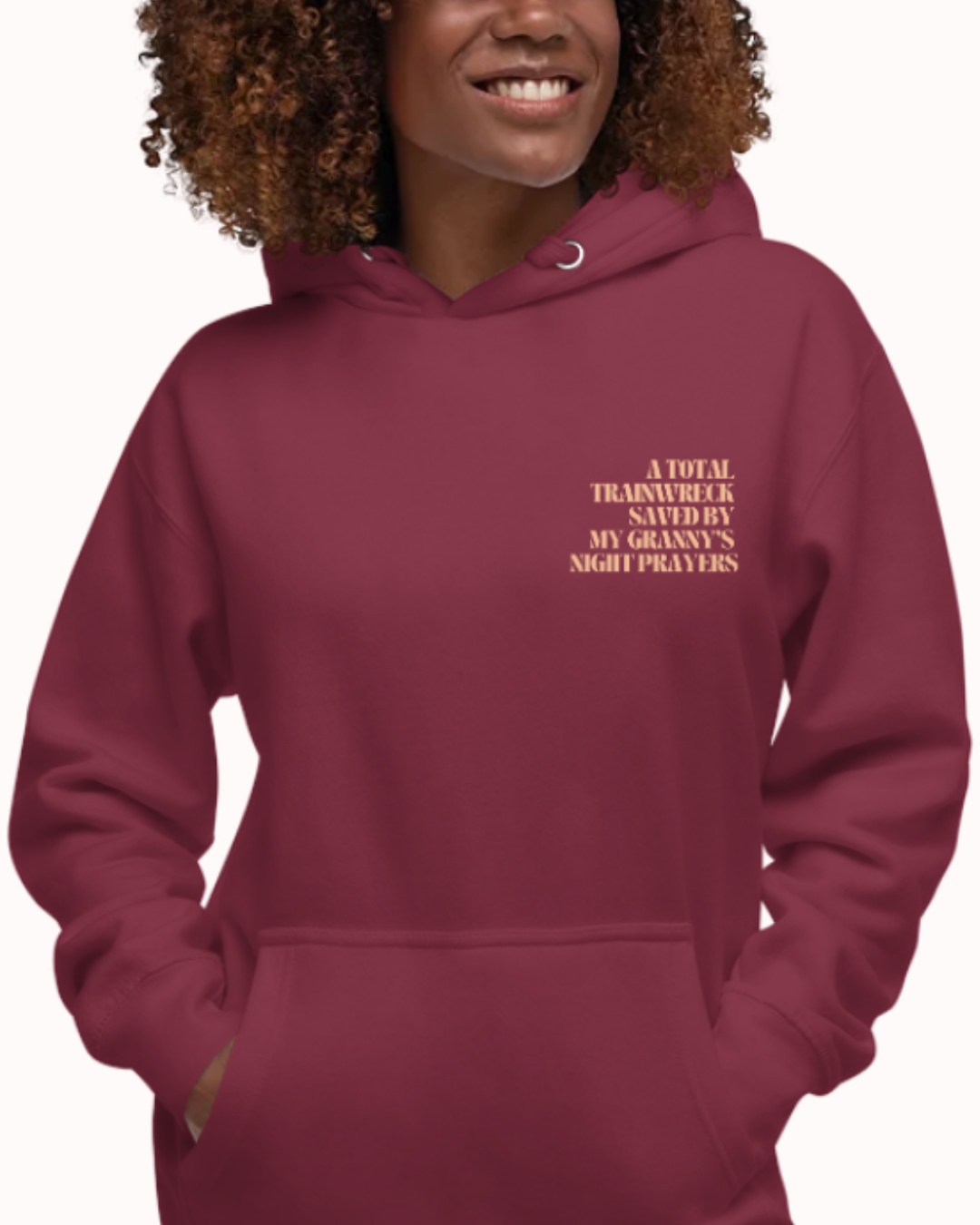 Front view of a Maroon hoodie worn by a smiling woman, featuring the phrase "A total trainwreck saved my granny's night prayers" on the chest and back. Perfect for fans of funny merchandise, bold humor, and witty sarcasm.