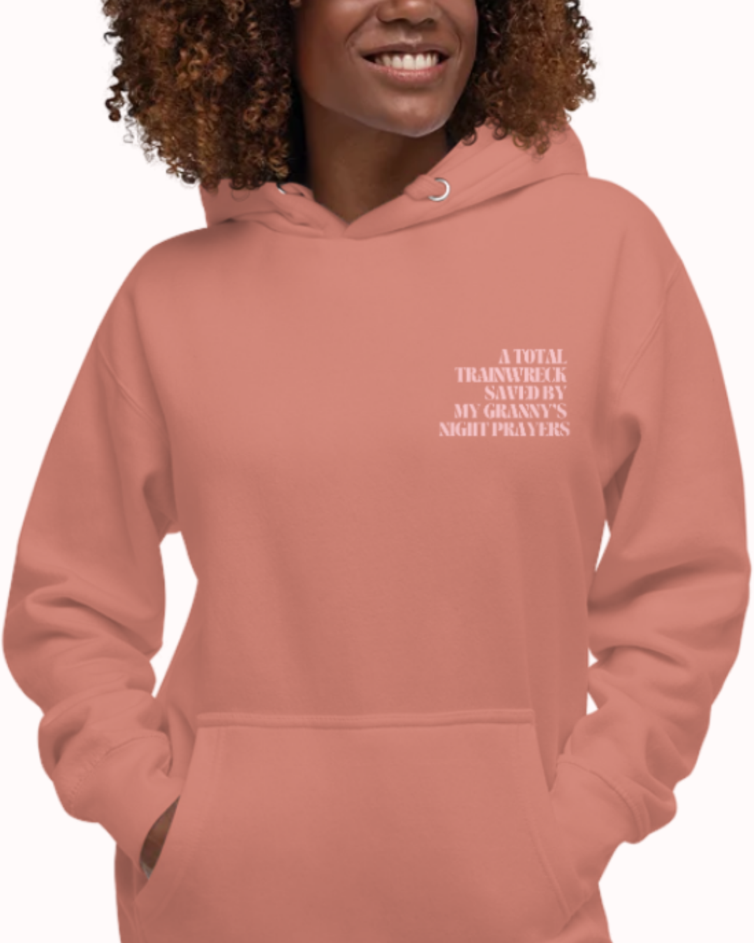 Front view of a Dusty Rose hoodie worn by a smiling woman, featuring the phrase "A total trainwreck saved my granny's night prayers" on the chest and back. Perfect for fans of funny merchandise, bold humor, and witty sarcasm.