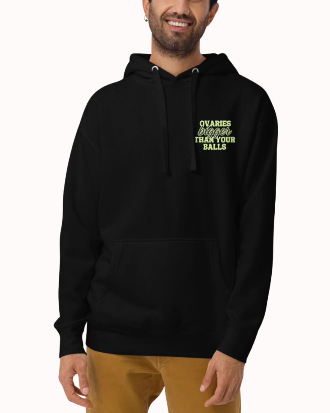 Front view of a black hoodie worn by a smiling man, featuring the phrase 'Ovaries bigger than your balls' on the chest and back. Perfect for fans of funny merchandise, bold humor, and witty sarcasm.
