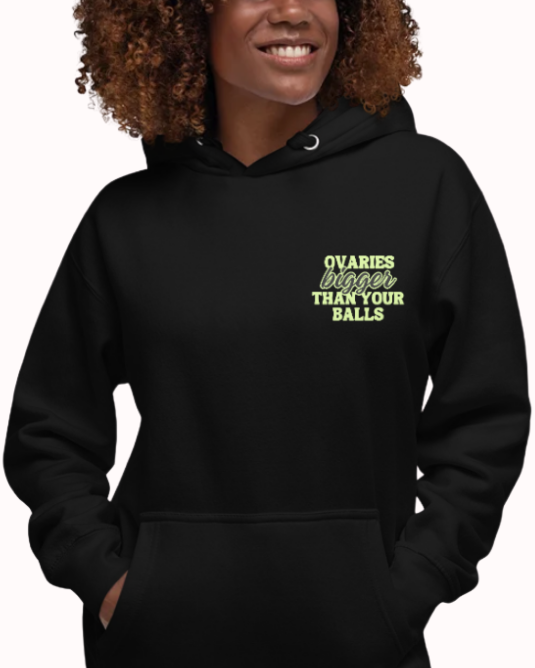 Front view of a black hoodie worn by a smiling woman, featuring the phrase 'Ovaries bigger than your balls' on the chest and back. Perfect for fans of funny merchandise, bold humor, and witty sarcasm.