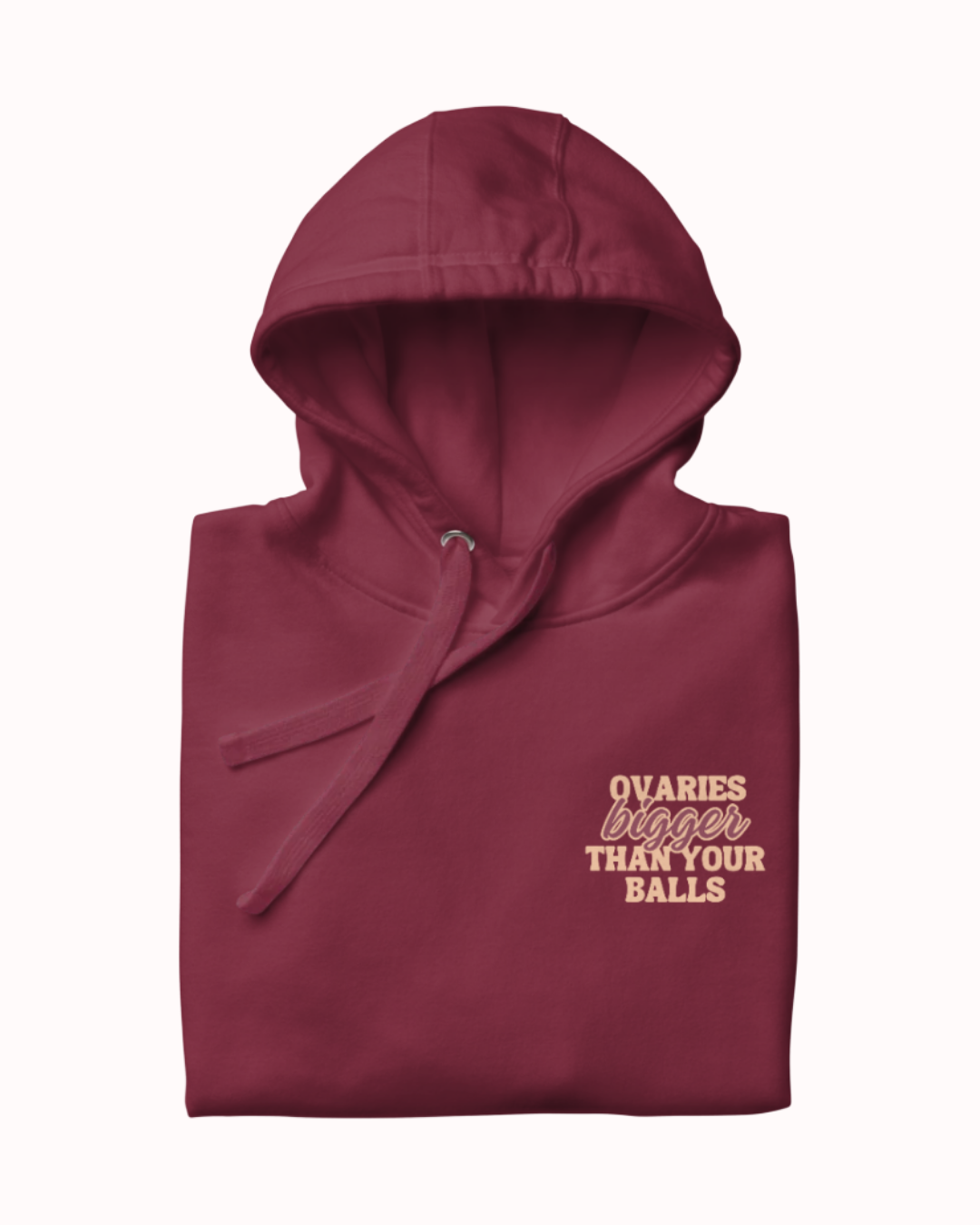Folded maroon hoodie featuring the ironic phrase 'Ovaries bigger than your balls'. Perfect for fans of funny merchandise, bold humor, and witty sarcasm.
