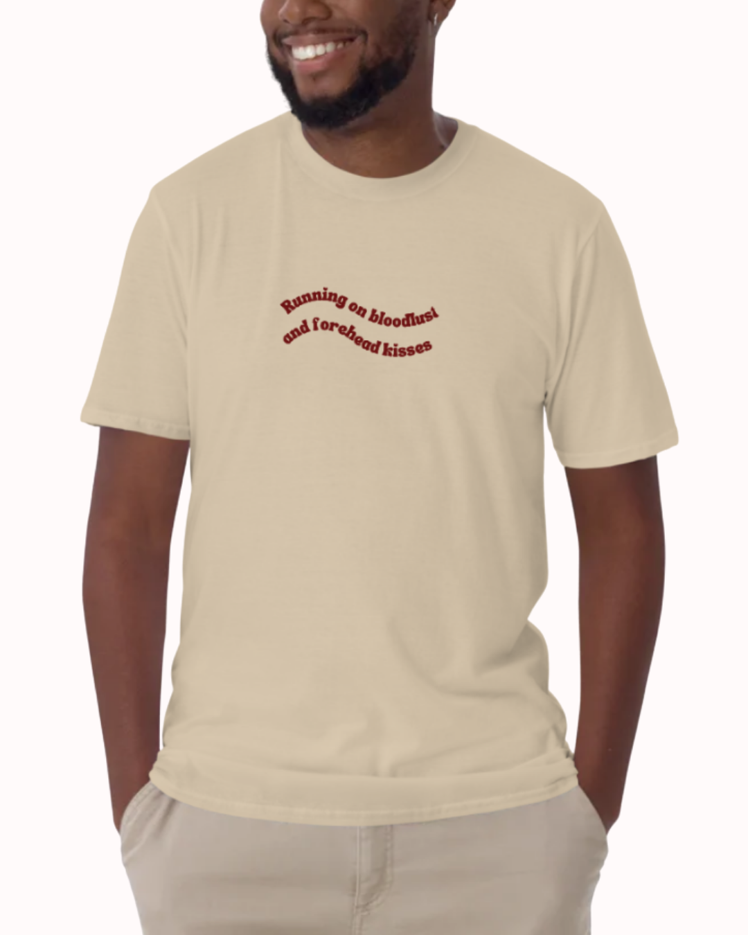 Front view of a Sand t-shirt worn by a smiling man, featuring the phrase "Running on bloodlust and forehead kisses" on the chest and back. Perfect for fans of funny merchandise, bold humor, and witty sarcasm.