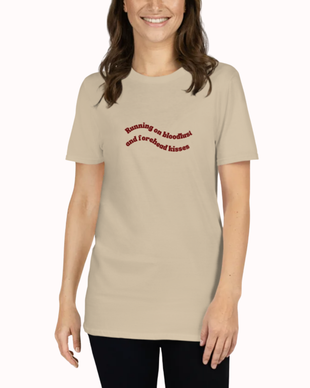 Front view of a Sand t-shirt worn by a smiling woman, featuring the phrase "Running on bloodlust and forehead kisses" on the chest and back. Perfect for fans of funny merchandise, bold humor, and witty sarcasm.