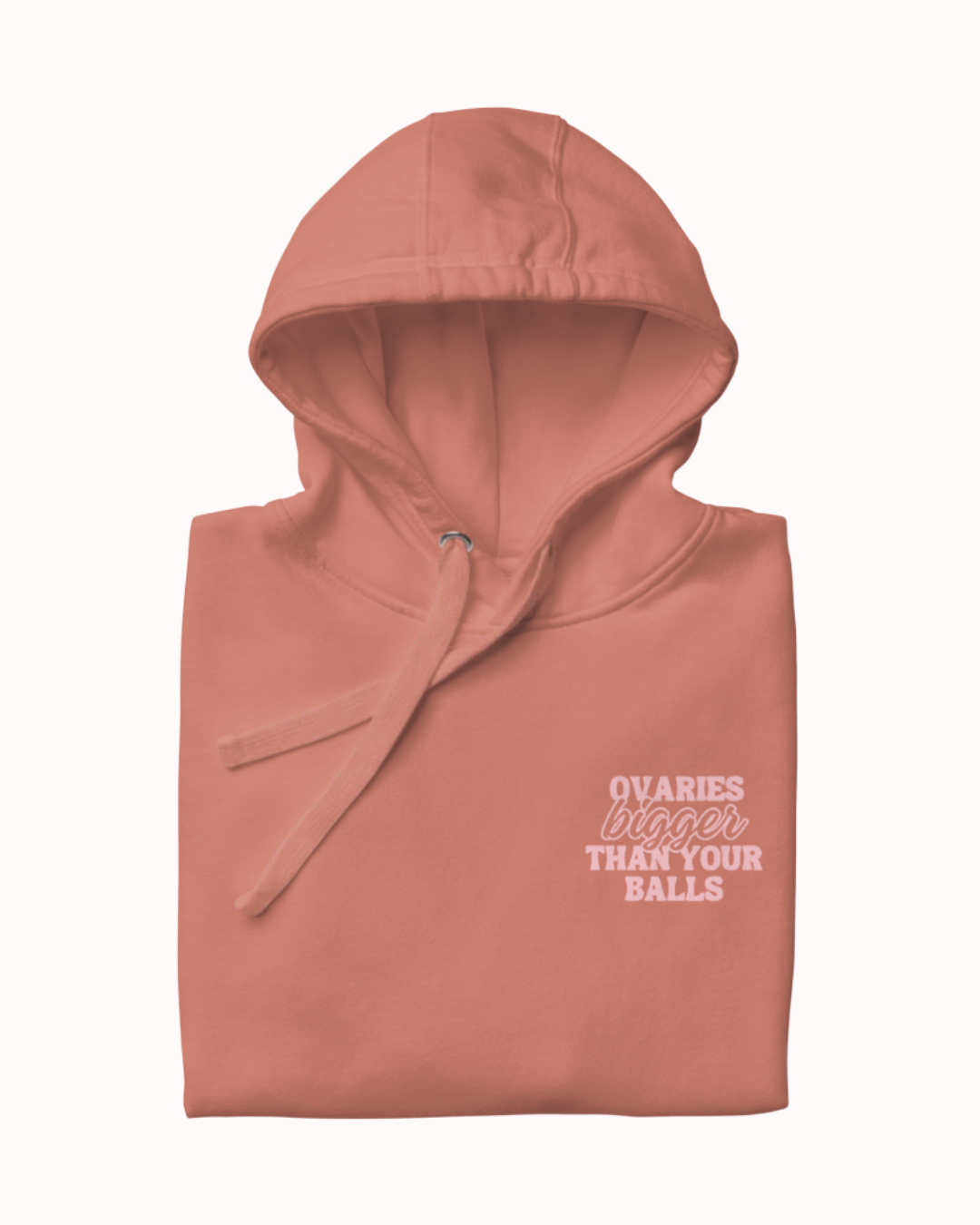 Folded dusty rose hoodie featuring the ironic phrase 'Ovaries bigger than your balls'. Perfect for fans of funny merchandise, bold humor, and witty sarcasm.