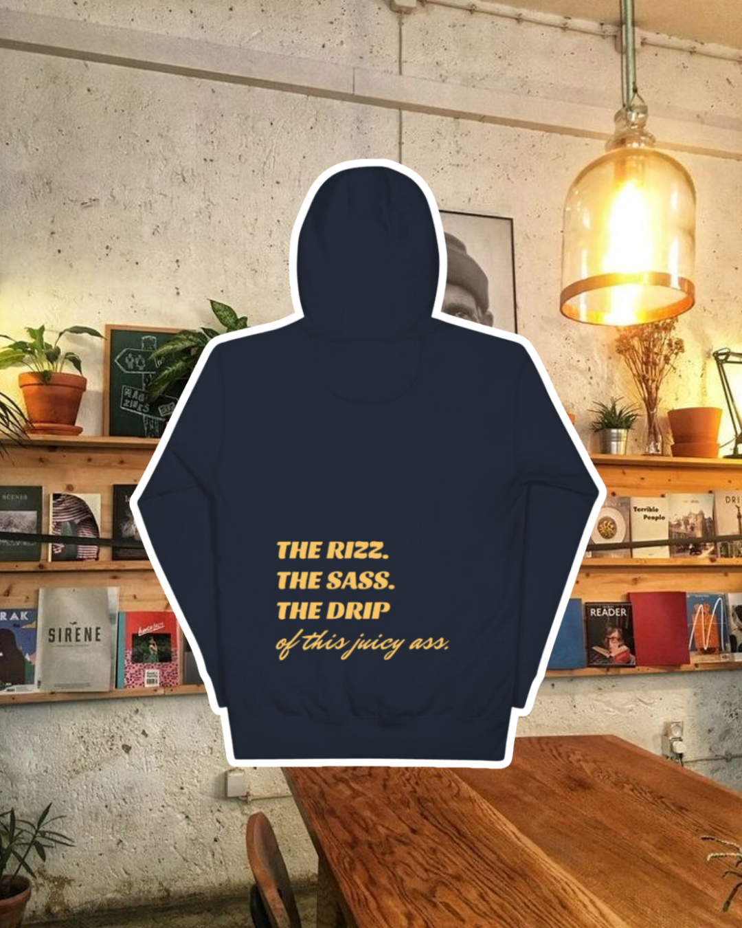 Navy blazer hoodie with the phrase 'The Rizz. The Sass. The Drip of this Juicy Ass' on the back, displayed against a vibrant café-style backdrop with wood chairs and colorful cozy decoration. A playful and bold design for fans of funny merchandise and sarcasm.