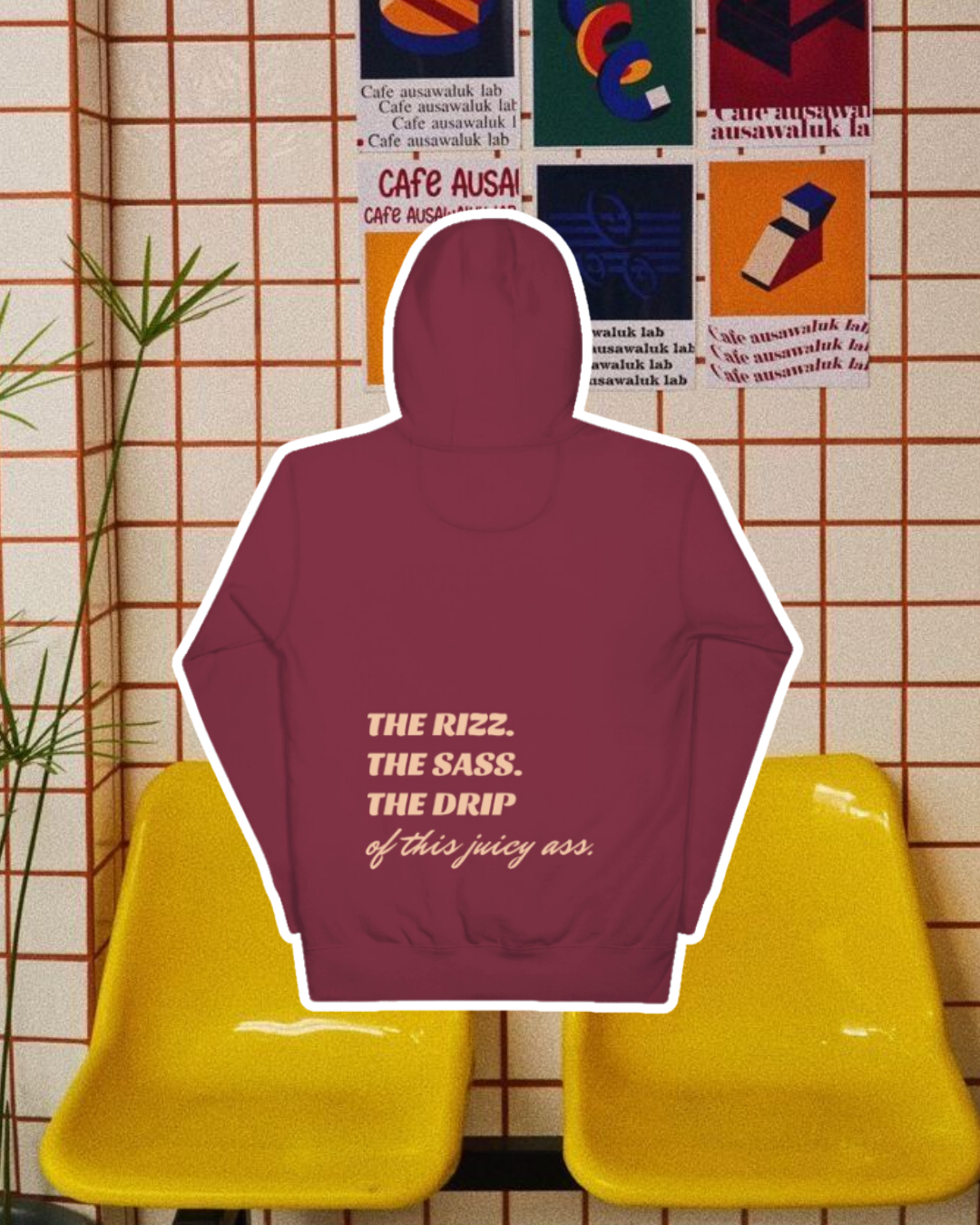 Maroon hoodie with the phrase 'The Rizz. The Sass. The Drip of this Juicy Ass' on the back, displayed against a vibrant café-style backdrop with yellow chairs and colorful posters. A playful and bold design for fans of funny merchandise and sarcasm.