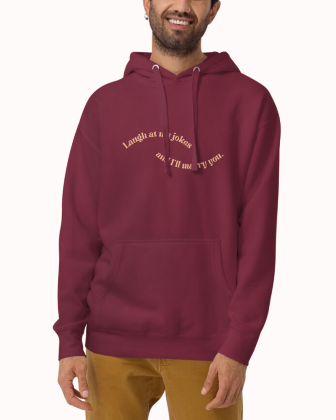 Front view of a maroon hoodie worn by a smiling man, featuring the phrase 'Laugh at my jokes and I'll marry you' on the chest. Perfect for fans of funny merchandise, bold humor, and witty sarcasm.