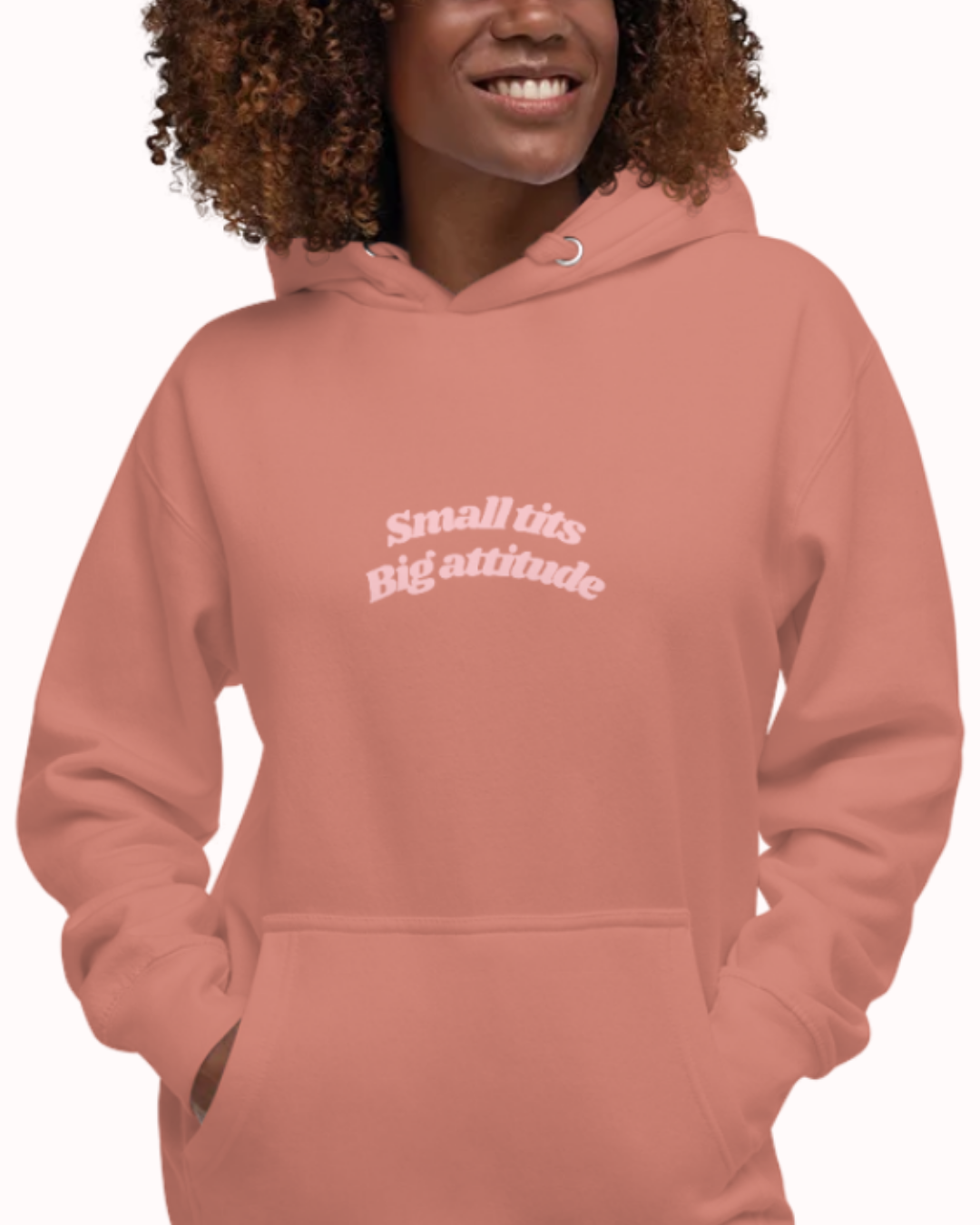 Front view of a Dusty Rose hoodie worn by a smiling woman, featuring the phrase "Small tits. Big attitude" on the chest and back. Perfect for fans of funny merchandise, bold humor, and witty sarcasm.