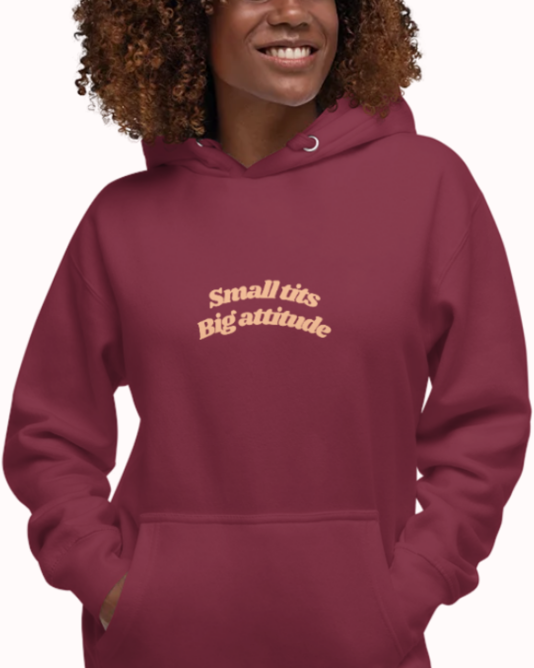 Front view of a Maroon hoodie worn by a smiling woman, featuring the phrase "Small tits. Big attitude" on the chest and back. Perfect for fans of funny merchandise, bold humor, and witty sarcasm.