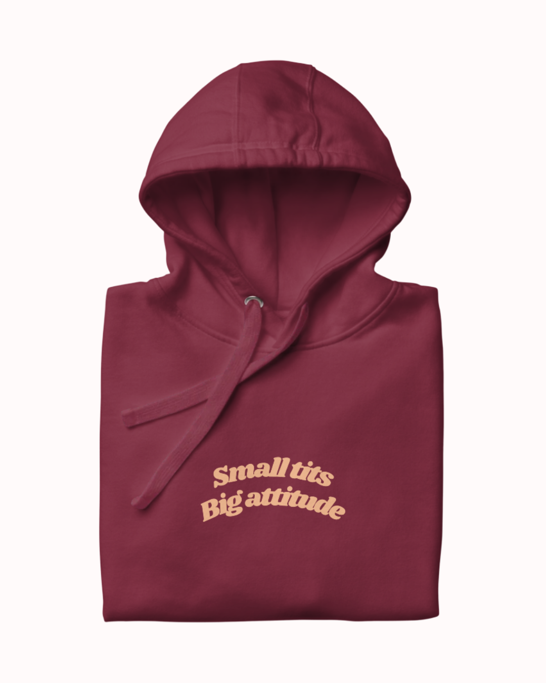 Folded Maroon hoodie featuring the ironic phrase "Small tits. Big attitude". Perfect for fans of funny merchandise, bold humor, and witty sarcasm.