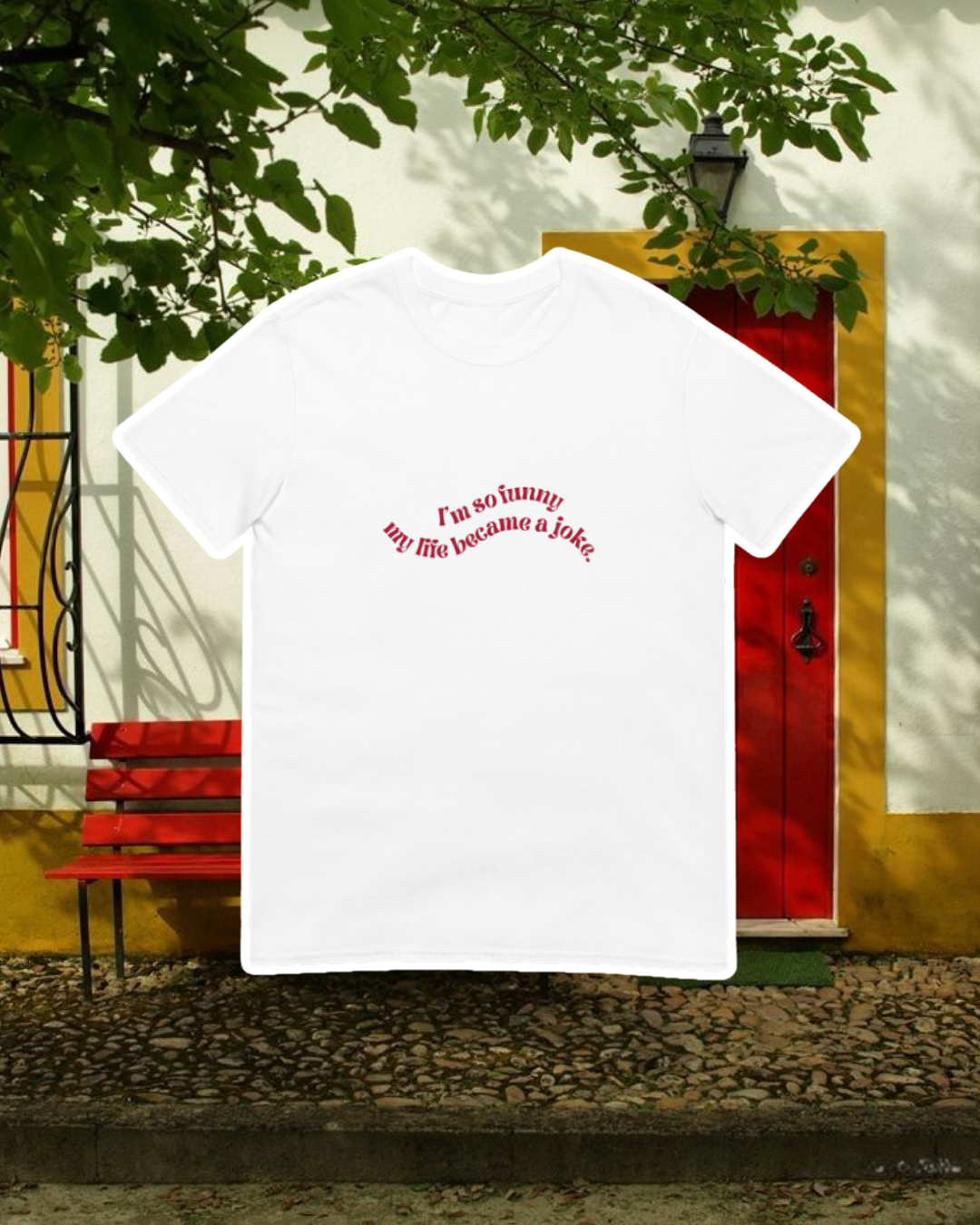 White T-Shirt with the phrase 'I'm so funny my life became a joke' on the chest, displayed against an inviting space, perfect for relaxation or gathering with friends. A playful and bold design for fans of funny merchandise and sarcasm.