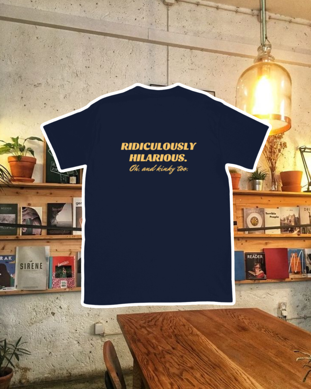 Navy T-Shirt with the phrase 'Ridiculously hilarious. Oh, and kinky too' on the back, displayed against a vibrant café-style backdrop with wood chairs and colorful cozy decoration. A playful and bold design for fans of funny merchandise and sarcasm.