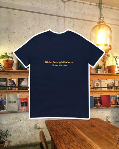 Navy T-Shirt with the phrase 'Ridiculously hilarious. Oh, and kinky too' on the chest, displayed against a vibrant café-style backdrop with wood chairs and colorful cozy decoration. A playful and bold design for fans of funny merchandise and sarcasm.