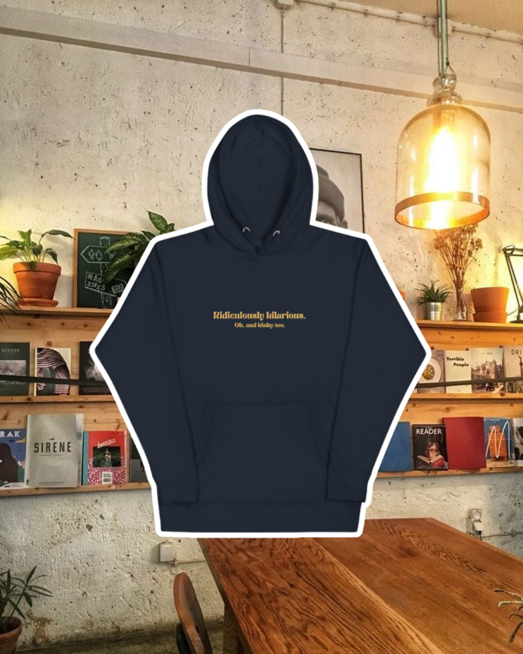 Navy blazer hoodie with the phrase 'Ridiculously hilarious. Oh, and kinky too' on the chest, displayed against a vibrant café-style backdrop with wood chairs and colorful cozy decoration. A playful and bold design for fans of funny merchandise and sarcasm.