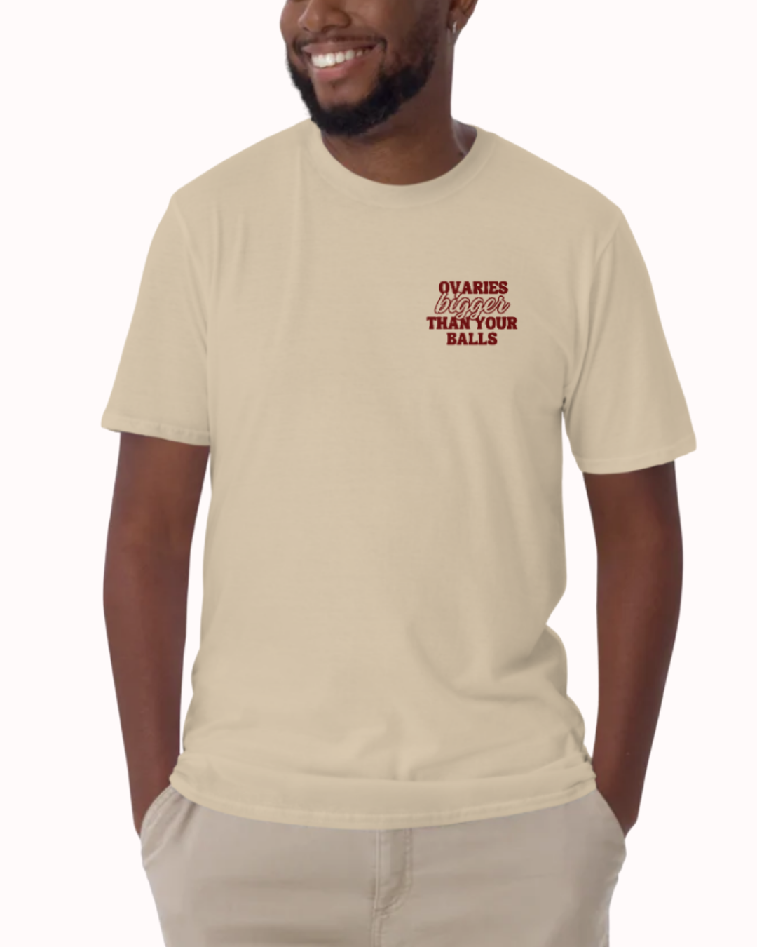 Front view of a Sand t-shirt worn by a smiling man, featuring the phrase "Ovaries bigger than your balls" on the chest and back. Perfect for fans of funny merchandise, bold humor, and witty sarcasm.
