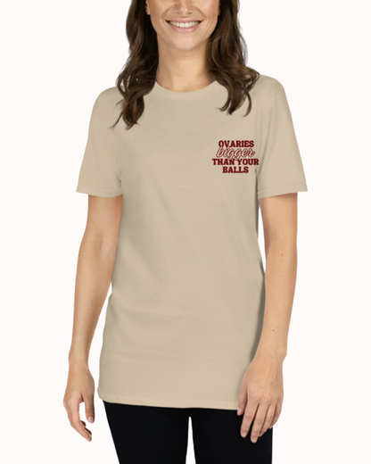 Front view of a Sand t-shirt worn by a smiling woman, featuring the phrase "Ovaries bigger than your balls" on the chest and back. Perfect for fans of funny merchandise, bold humor, and witty sarcasm.