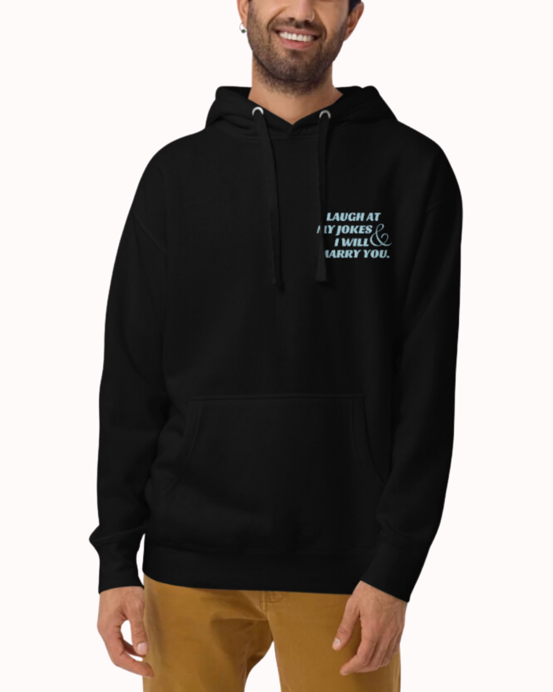 Front view of a black hoodie worn by a smiling man, featuring the phrase 'Laugh at my jokes and I will marry you' on the chest and back. Perfect for fans of funny merchandise, bold humor, and witty sarcasm.