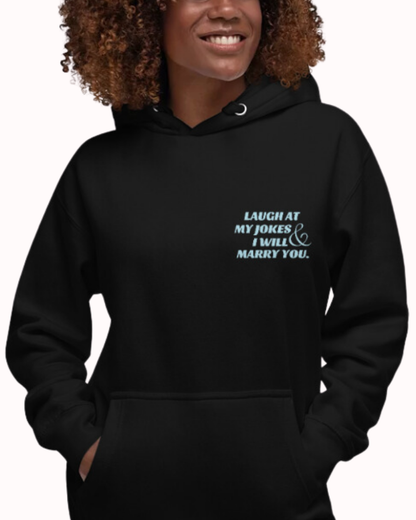 Front view of a black hoodie worn by a smiling woman, featuring the phrase 'Laugh at my jokes and I will marry you' on the chest and back. Perfect for fans of funny merchandise, bold humor, and witty sarcasm.