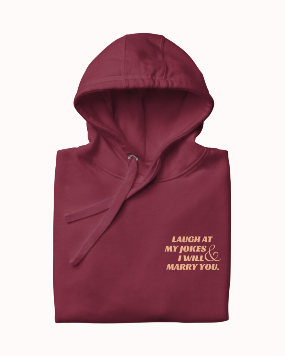 Folded maroon hoodie featuring the ironic phrase 'Laugh at my jokes and I will marry you'. Perfect for fans of funny merchandise, bold humor, and witty sarcasm. 