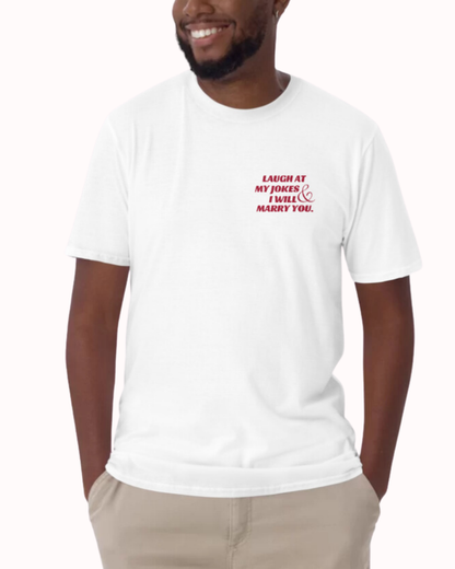 Front view of a white T-Shirt worn by a smiling man, featuring the phrase 'Laugh at my jokes and I will marry you' on the chest and back. Perfect for fans of funny merchandise, bold humor, and witty sarcasm. 