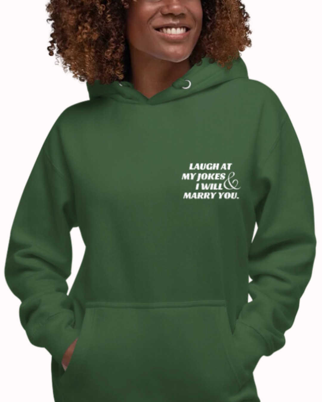 Front view of a forest green hoodie worn by a smiling woman, featuring the phrase 'Laugh at my jokes and I will marry you' on the chest and back. Perfect for fans of funny merchandise, bold humor, and witty sarcasm.