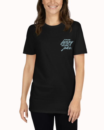 Front view of a black T-Shirt worn by a smiling woman, featuring the phrase 'I'm so funny my life became a joke' on the chest and back. Perfect for fans of funny merchandise, bold humor, and witty sarcasm.