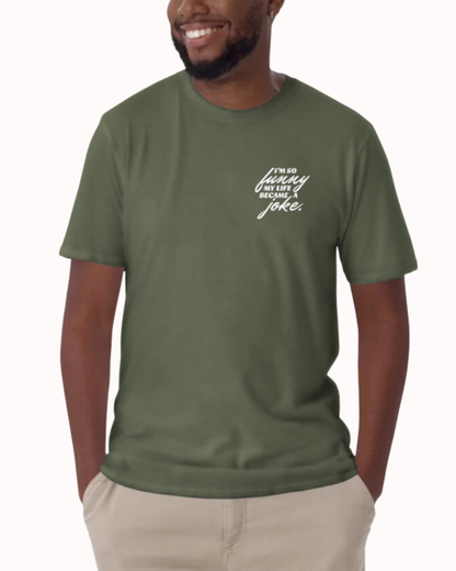 Front view of a military green T-Shirt worn by a smiling man, featuring the phrase 'I'm so funny my life became a joke' on the chest and back. Perfect for fans of funny merchandise, bold humor, and witty sarcasm. 