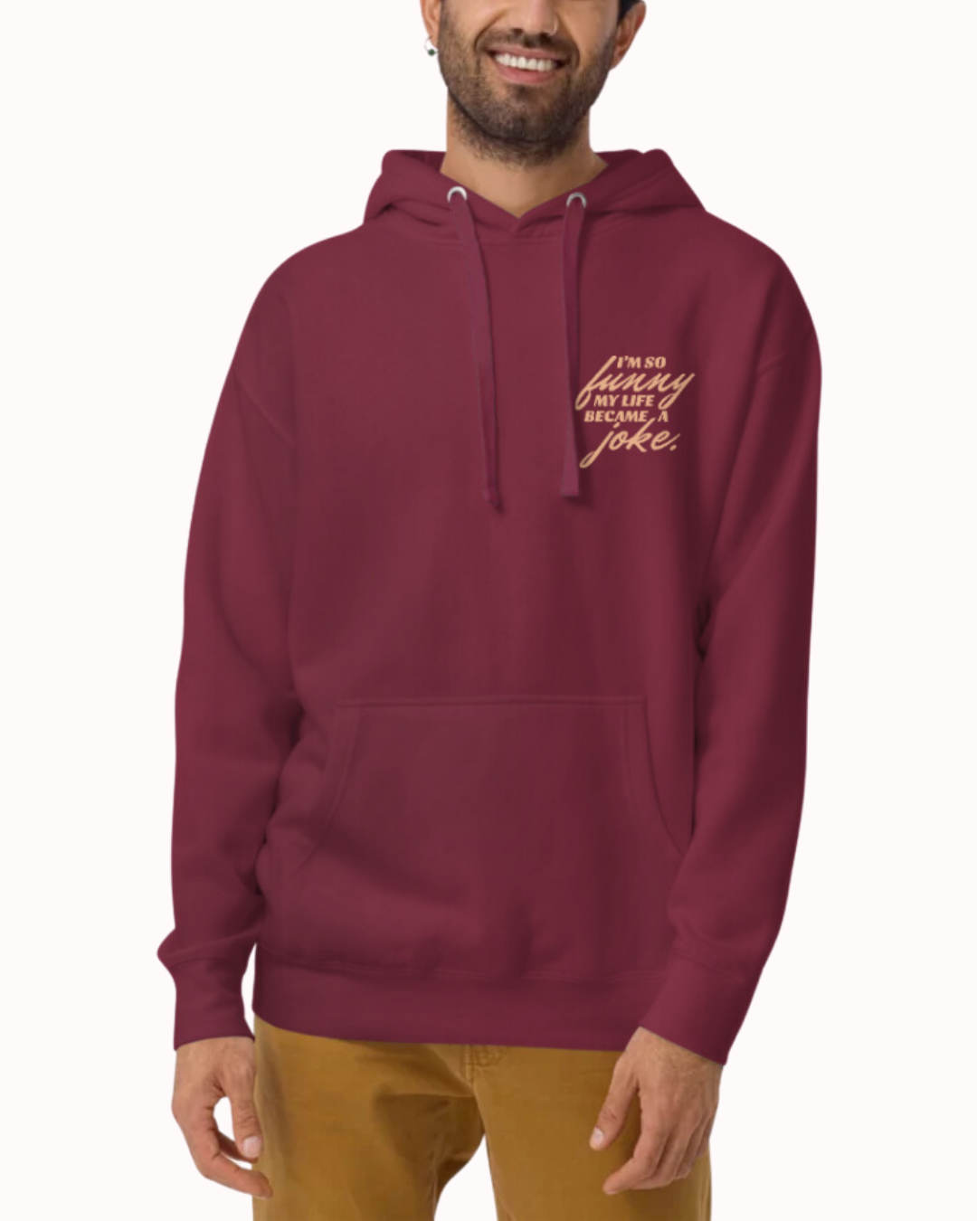 Front view of a maroon hoodie worn by a smiling man, featuring the phrase 'I'm so funny my life became a joke' on the chest and back. Perfect for fans of funny merchandise, bold humor, and witty sarcasm.