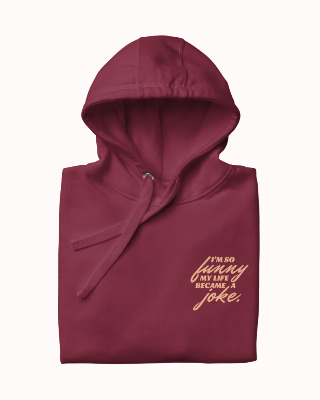 Folded maroon hoodie featuring the ironic phrase 'I'm so funny my life became a joke'. Perfect for fans of funny merchandise, bold humor, and witty sarcasm. 