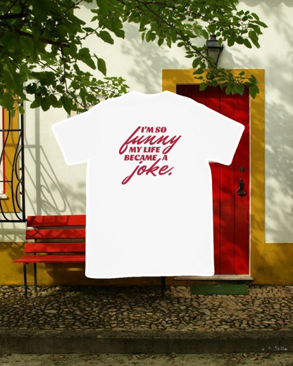 White T-Shirt with the phrase 'I'm so funny my life became a joke' on the back, displayed against an inviting space, perfect for relaxation or gathering with friends. A playful and bold design for fans of funny merchandise and sarcasm. 