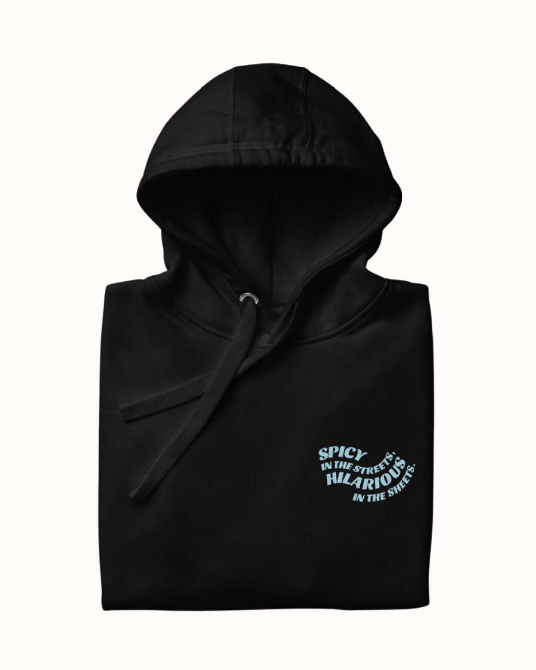 Folded black hoodie featuring the ironic phrase 'Spicy in the streets, Hilarious in the sheets'. Perfect for fans of funny merchandise, bold humor, and witty sarcasm.