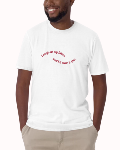 Front view of a white T-Shirt worn by a smiling man, featuring the phrase 'Laugh at my jokes and I will marry you' on the chest. Perfect for fans of funny merchandise, bold humor, and witty sarcasm. 