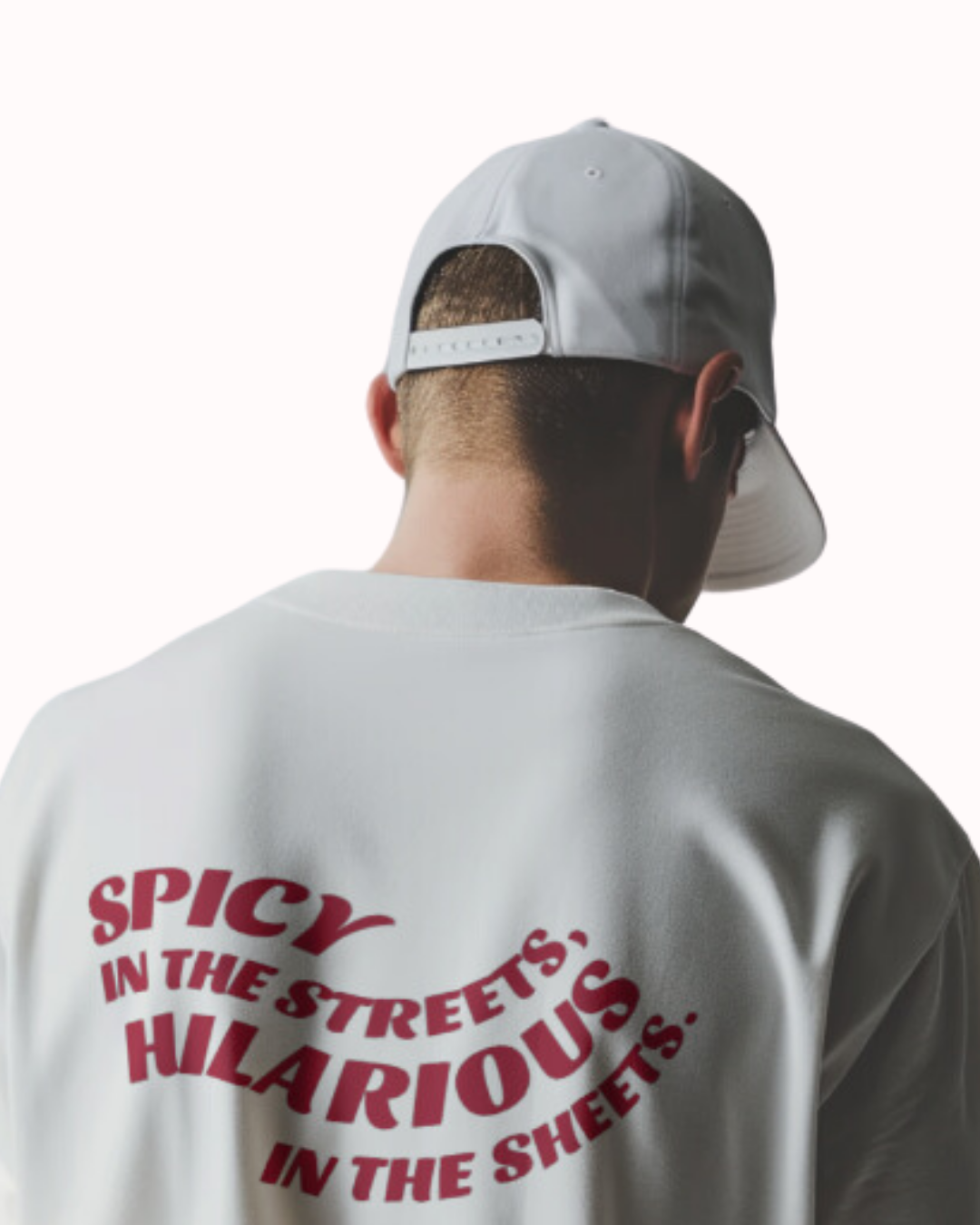 Back view of a white T-Shirt featuring the phrase 'Spicy in the streets, Hilarious in the sheets' on the back. Perfect for fans of funny merchandise, bold humor, and witty sarcasm.