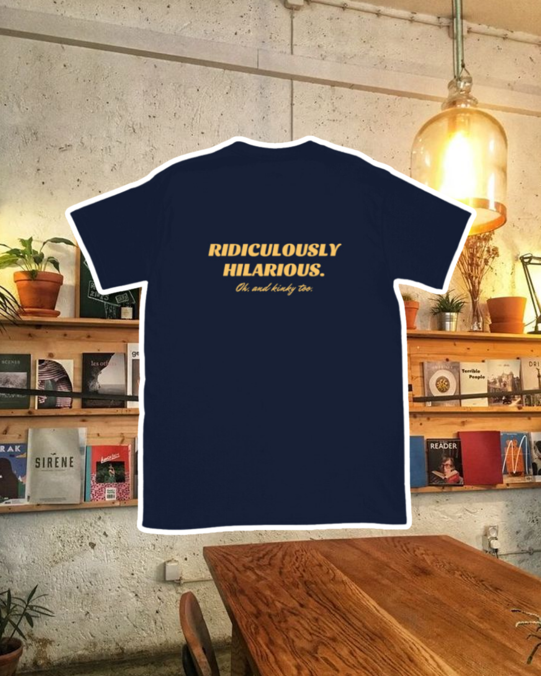 Navy T-Shirt with the phrase 'Ridiculously hilarious. Oh, and kinky too' on the back, displayed against a vibrant café-style backdrop with wood chairs and colorful cozy decoration. A playful and bold design for fans of funny merchandise and sarcasm.