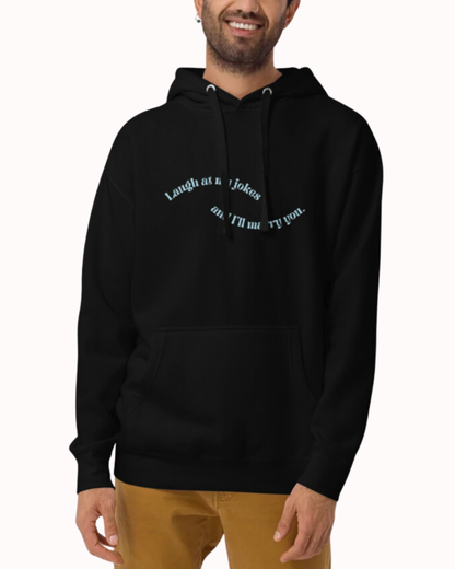 Front view of a black hoodie worn by a smiling man, featuring the phrase 'Laugh at my jokes and I'll marry you' on the chest. Perfect for fans of funny merchandise, bold humor, and witty sarcasm.