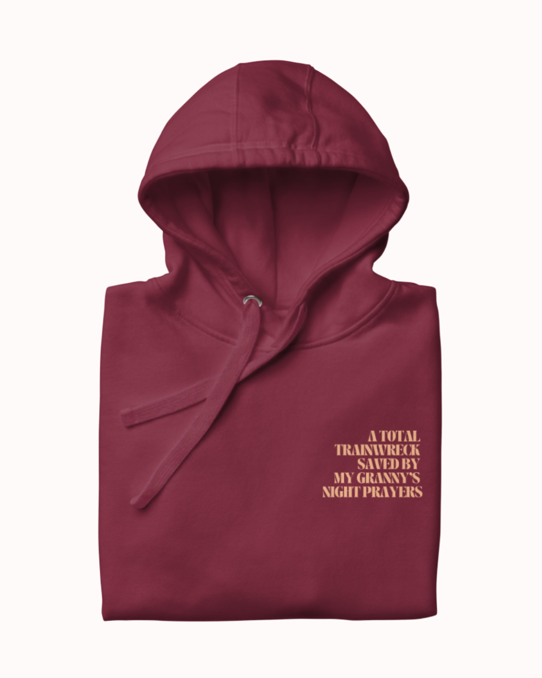 Folded Maroon hoodie featuring the ironic phrase "A total trainwreck saved my granny's night prayers". Perfect for fans of funny merchandise, bold humor, and witty sarcasm.