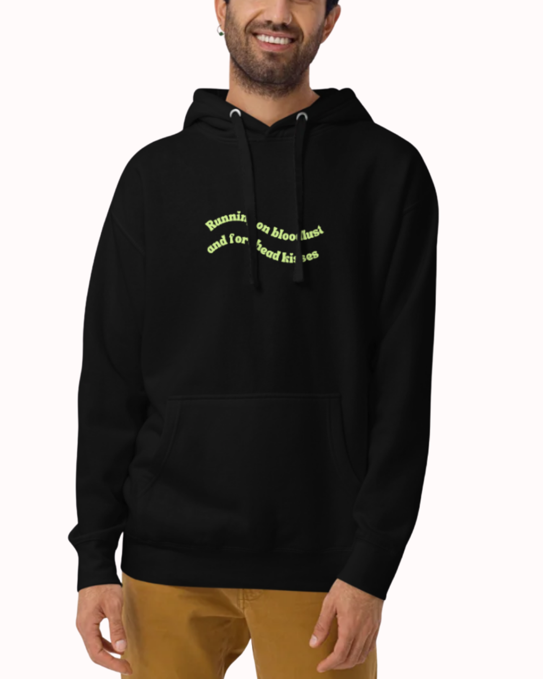 Front view of a Black hoodie worn by a smiling man, featuring the phrase "Running on bloodlust and forehead kisses" on the chest and back. Perfect for fans of funny merchandise, bold humor, and witty sarcasm.