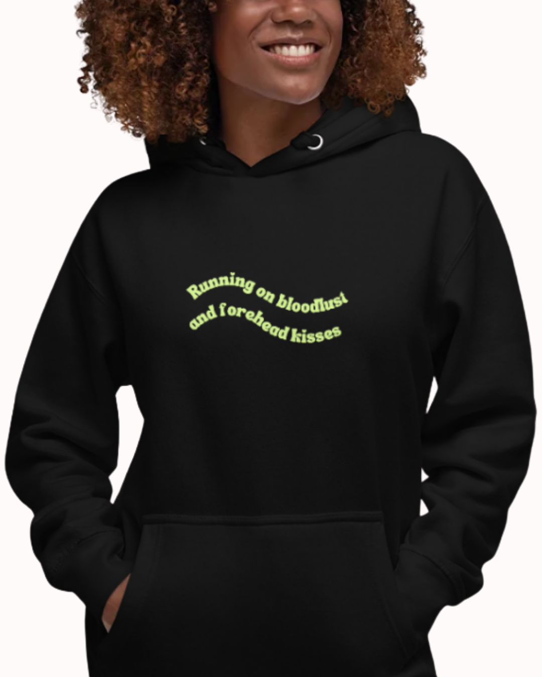 Front view of a Black hoodie worn by a smiling woman, featuring the phrase "Running on bloodlust and forehead kisses" on the chest and back. Perfect for fans of funny merchandise, bold humor, and witty sarcasm.