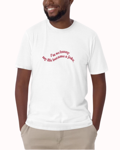 Front view of a white T-Shirt worn by a smiling man, featuring the phrase 'I'm so funny my life became a joke' on the chest. Perfect for fans of funny merchandise, bold humor, and witty sarcasm