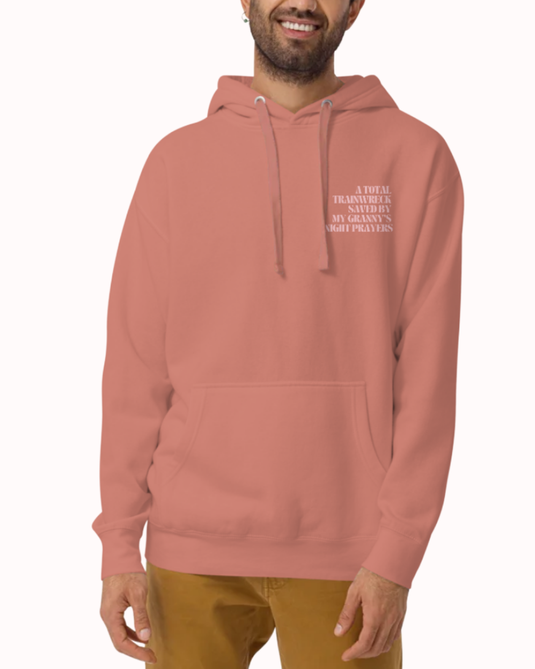 Front view of a Dusty Rose hoodie worn by a smiling man, featuring the phrase "A total trainwreck saved my granny's night prayers" on the chest and back. Perfect for fans of funny merchandise, bold humor, and witty sarcasm.