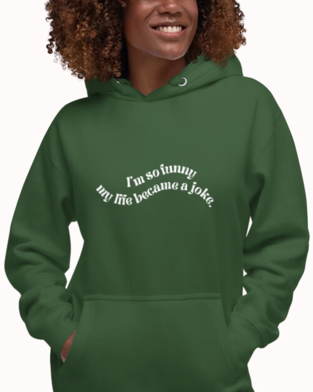 Front view of a forest green hoodie worn by a smiling woman, featuring the phrase 'I'm so funny my life became a joke' on the chest. Perfect for fans of funny merchandise, bold humor, and witty sarcasm.