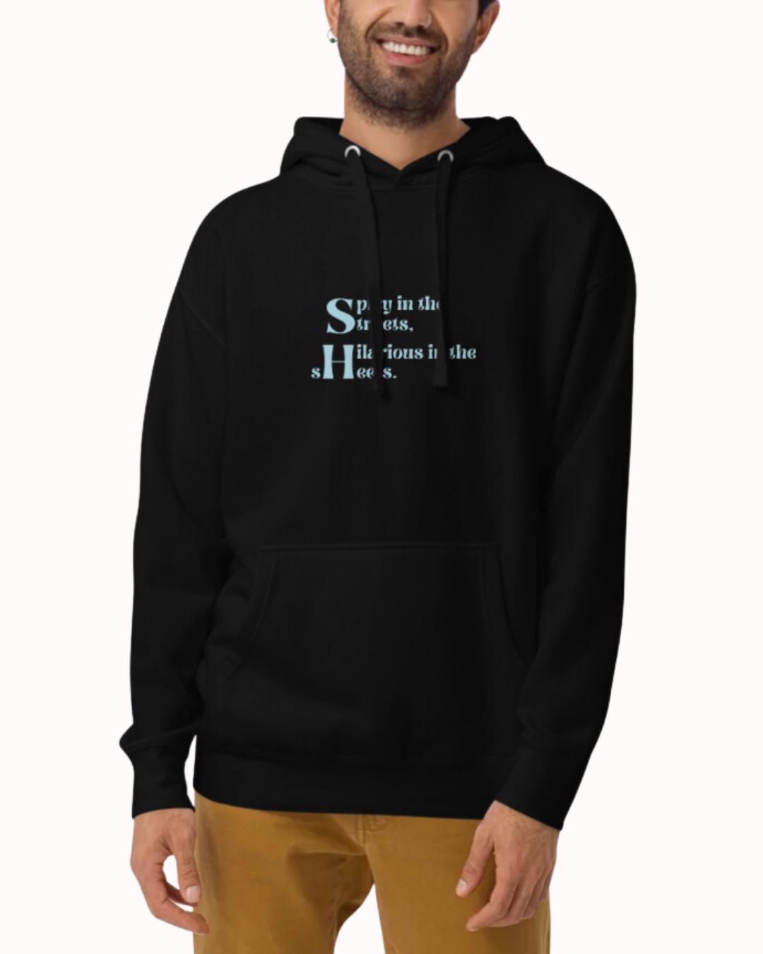 Front view of a black hoodie worn by a smiling man, featuring the phrase 'Spicy in the streets, Hilarious in the sheets' on the chest. Perfect for fans of funny merchandise, bold humor, and witty sarcasm.