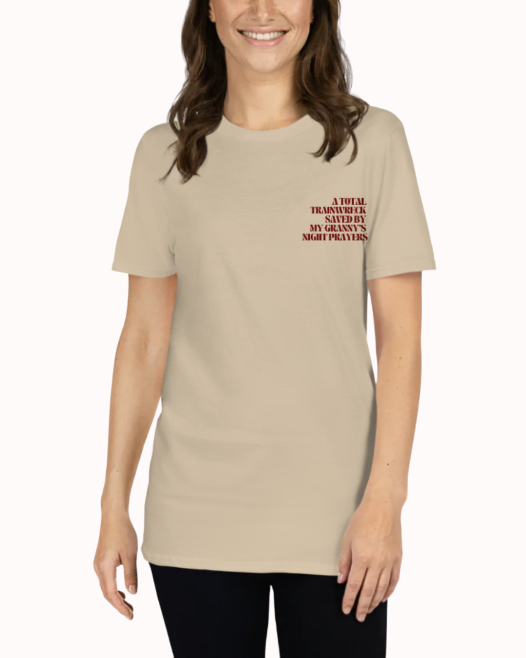 Front view of a Sand t-shirt worn by a smiling woman, featuring the phrase "A total trainwreck saved my granny's night prayers" on the chest and back. Perfect for fans of funny merchandise, bold humor, and witty sarcasm.