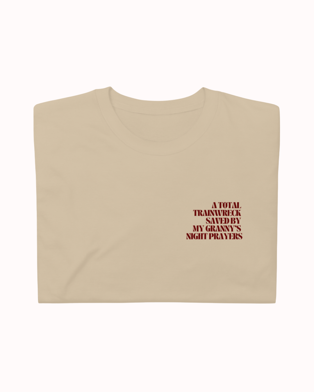 Folded Sand t-shirt featuring the ironic phrase "A total trainwreck saved my granny's night prayers". Perfect for fans of funny merchandise, bold humor, and witty sarcasm.