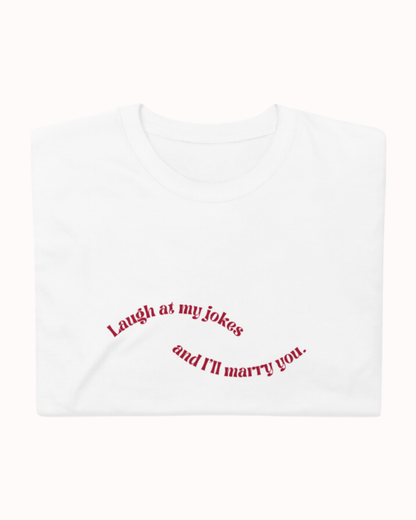 Folded white T-Shirt featuring the ironic phrase 'Laugh at my jokes and I will marry you'. Perfect for fans of funny merchandise, bold humor, and witty sarcasm. 